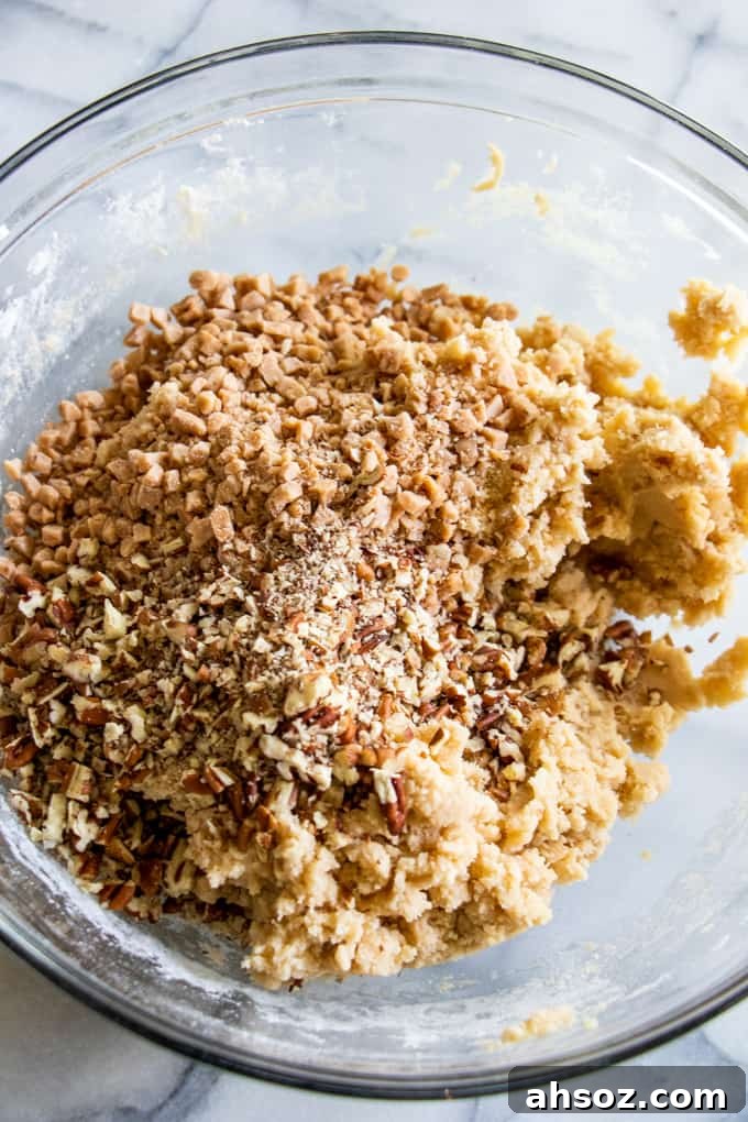 Bowl filled with butter pecan shortbread cookie dough topped with bits of chopped pecans and toffee bits.