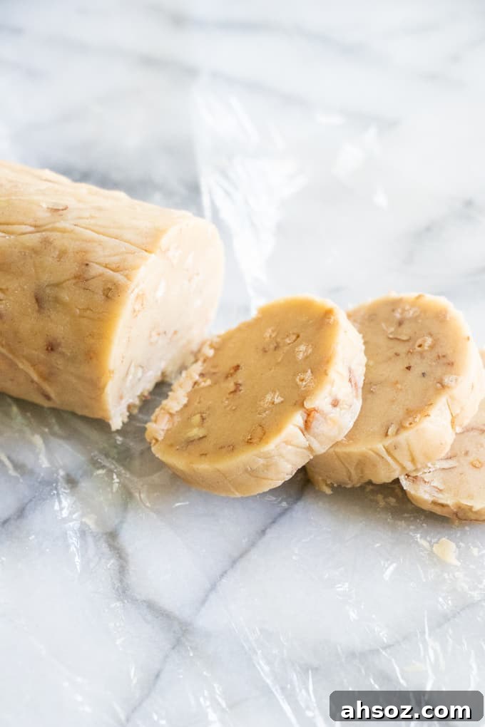 A roll of butter pecan shortbread cookies and slices being cut off to form into cookies.