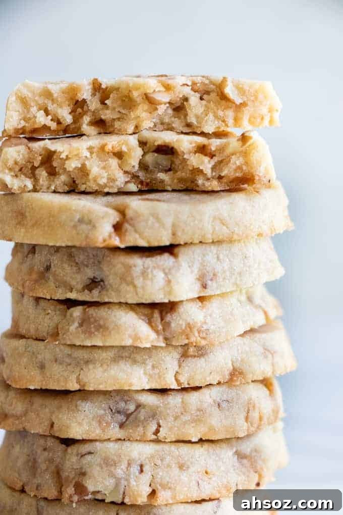 A stack of butter pecan shortbread cookies with bits of pecans and toffee bits around.