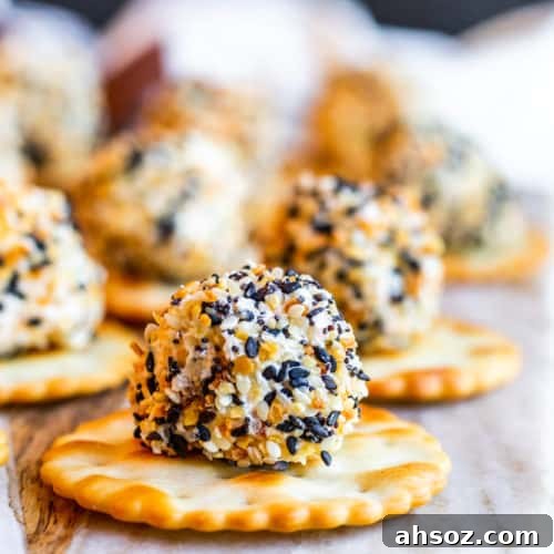 Cheese ball bite on a round cracker on a marble and wood cutting board.
