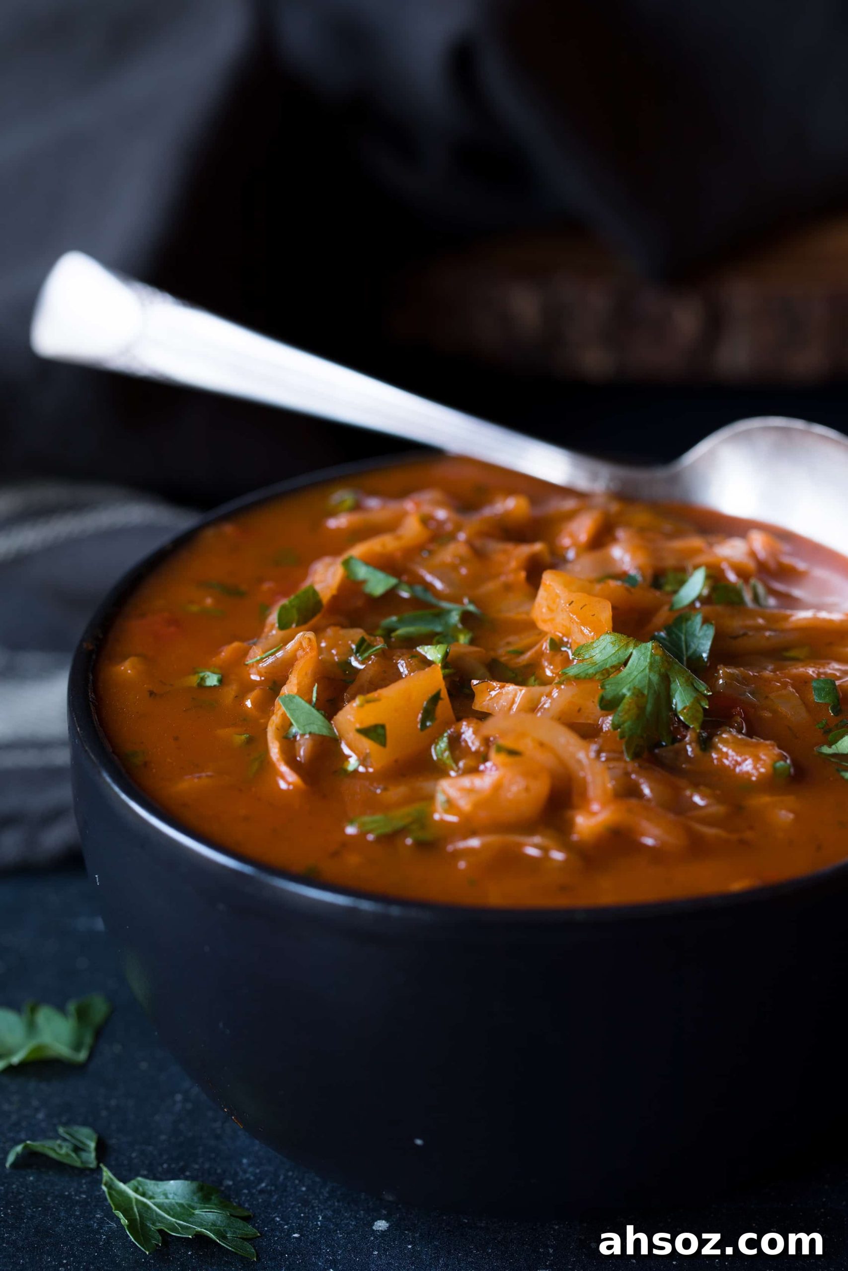 Close-up photo of Rustic Cabbage and Root Vegetable Soup in black bowl with spoon.