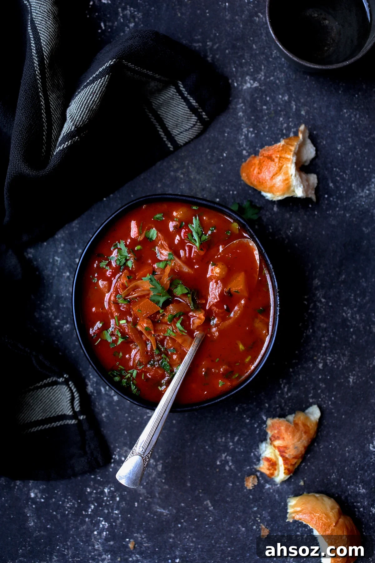 Rustic Cabbage and Root Vegetable Soup in black bowl garnished with parsley with pieces of bread scattered about.