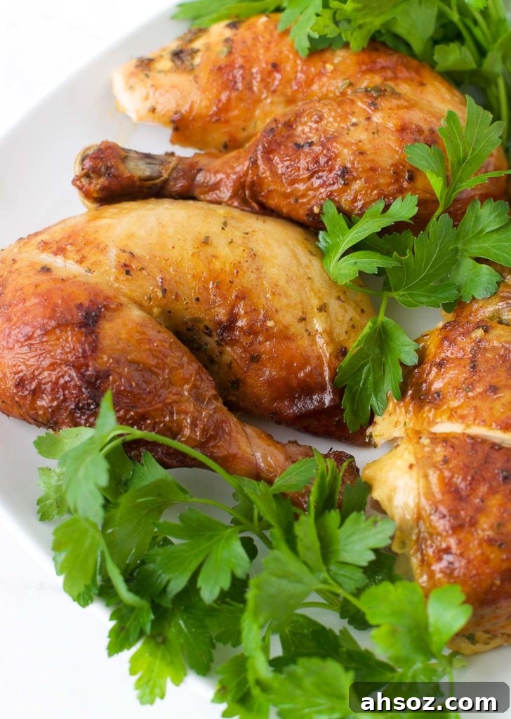 Close up of a Whole Roasted Chicken leg and other pieces sitting on greens on top of a white plate