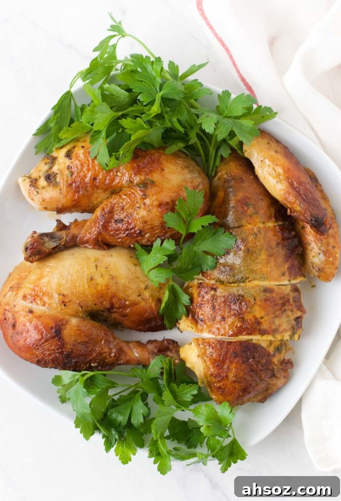 Sliced pieces of Oven Roasted Chicken sit on top of greens on a white plate