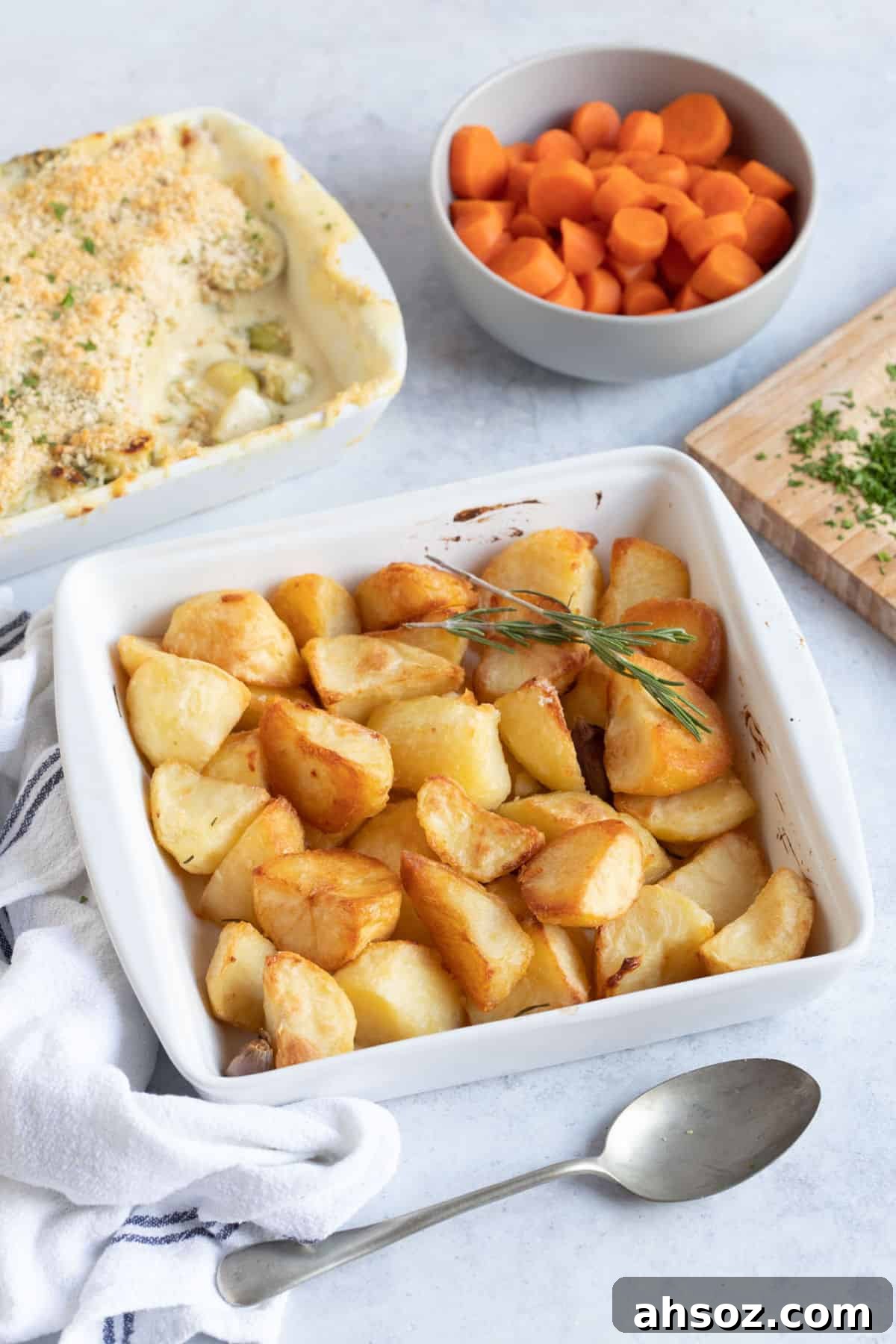 Duck fat roast potatoes in a white serving dish with a sprig of rosemary.