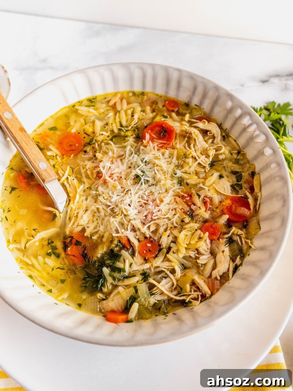Lemon chicken orzo soup garnished with herbs and parmesan cheese in a bowl.
