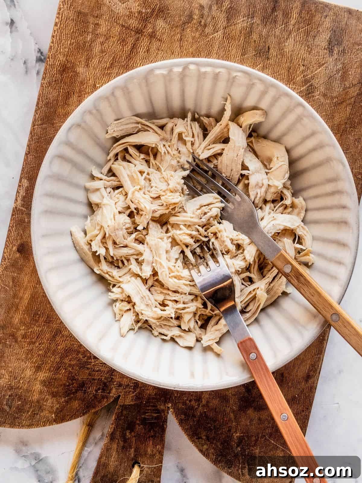 Recipe step showing the shredding of the chicken breast in a bowl with 2 forks.