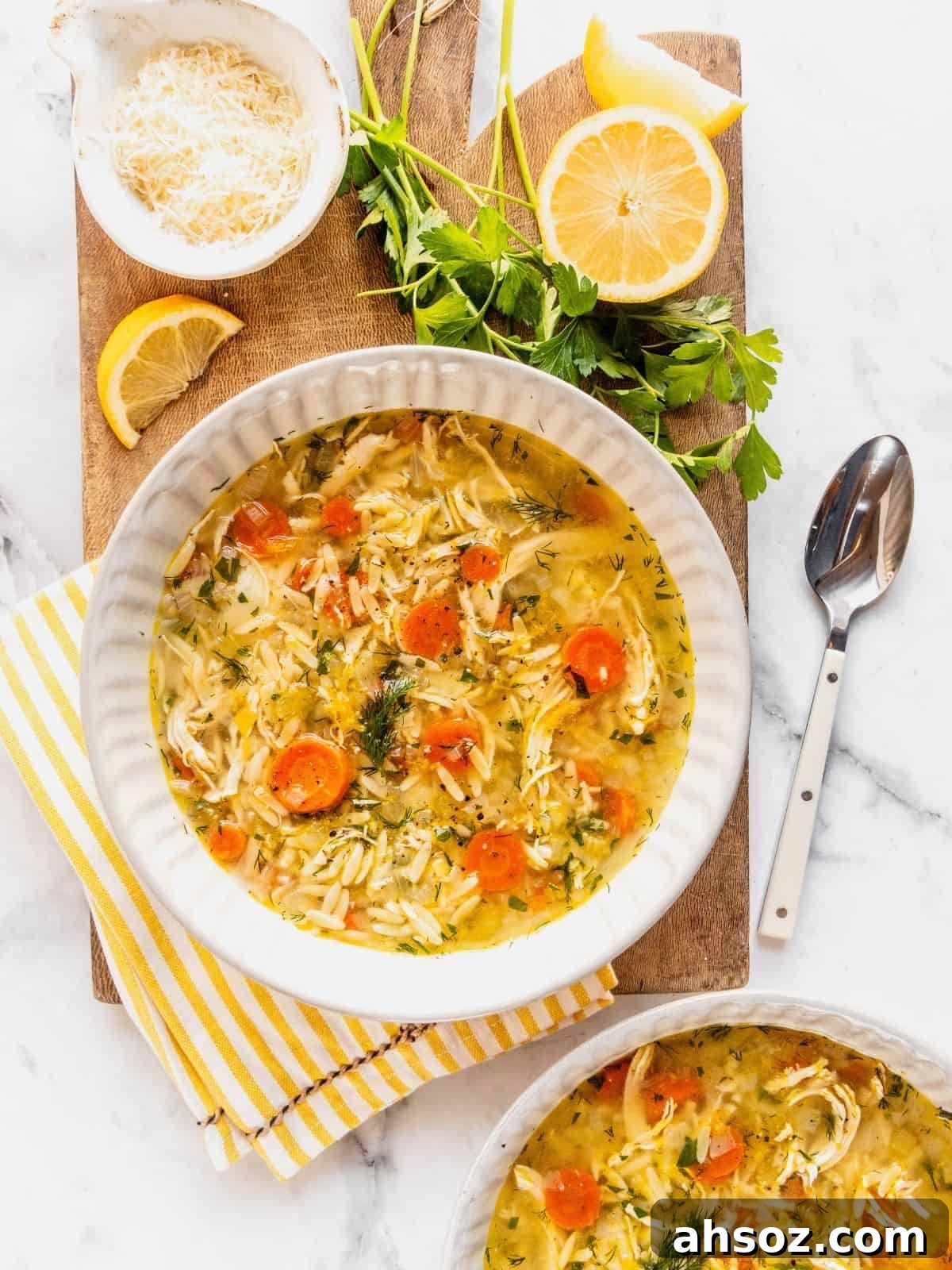 Lemon chicken orzo soup in a bowl with herbs and parmesan cheese garnishes on the side.