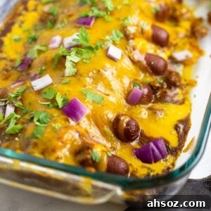 Chili cheese dog casserole in a glass 9-inch by 13-inch casserole dish topped with cilantro and red onions.