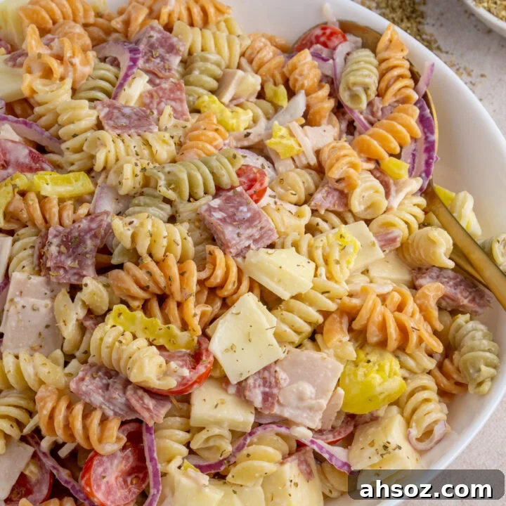 A white serving bowl filled with colorful grinder pasta salad with deli meats, cheeses, and veggies.