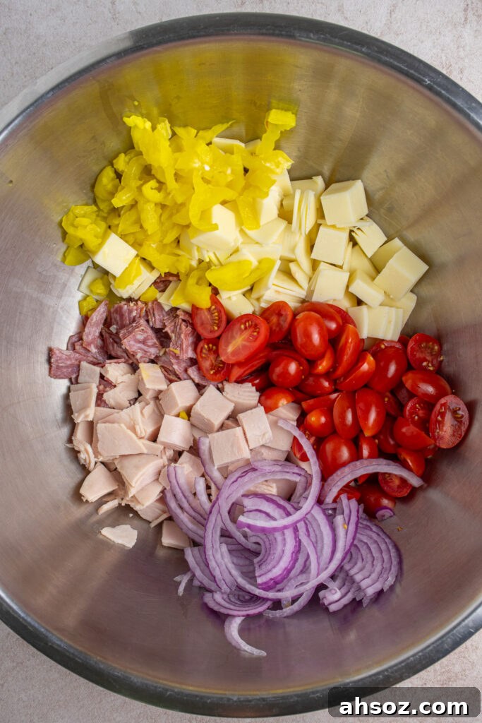 Making grinder pasta salad by adding all the chopped ingredients to a large bowl.