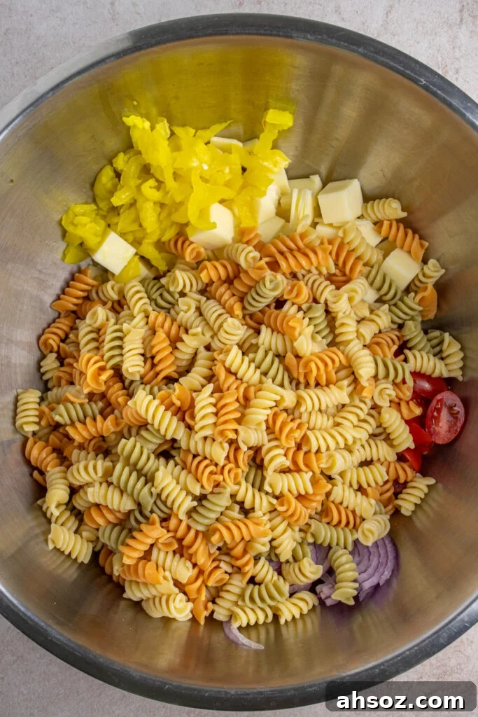Making grinder pasta salad by adding cooked pasta to a large bowl with the other ingredients.