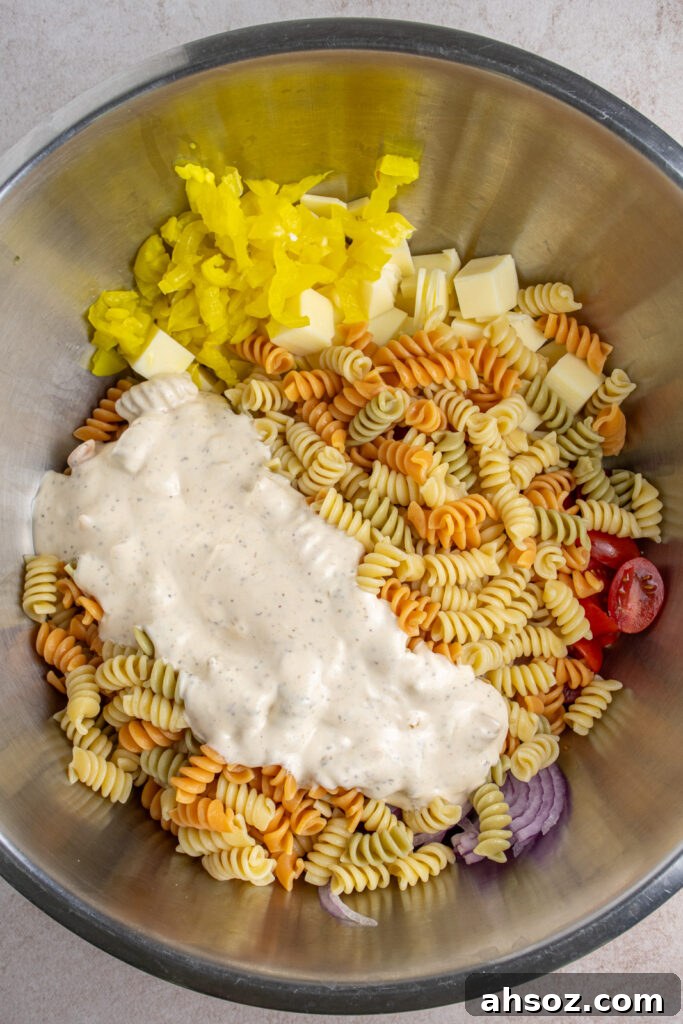 Adding dressing to a large bowl of ingredients for making grinder pasta salad.