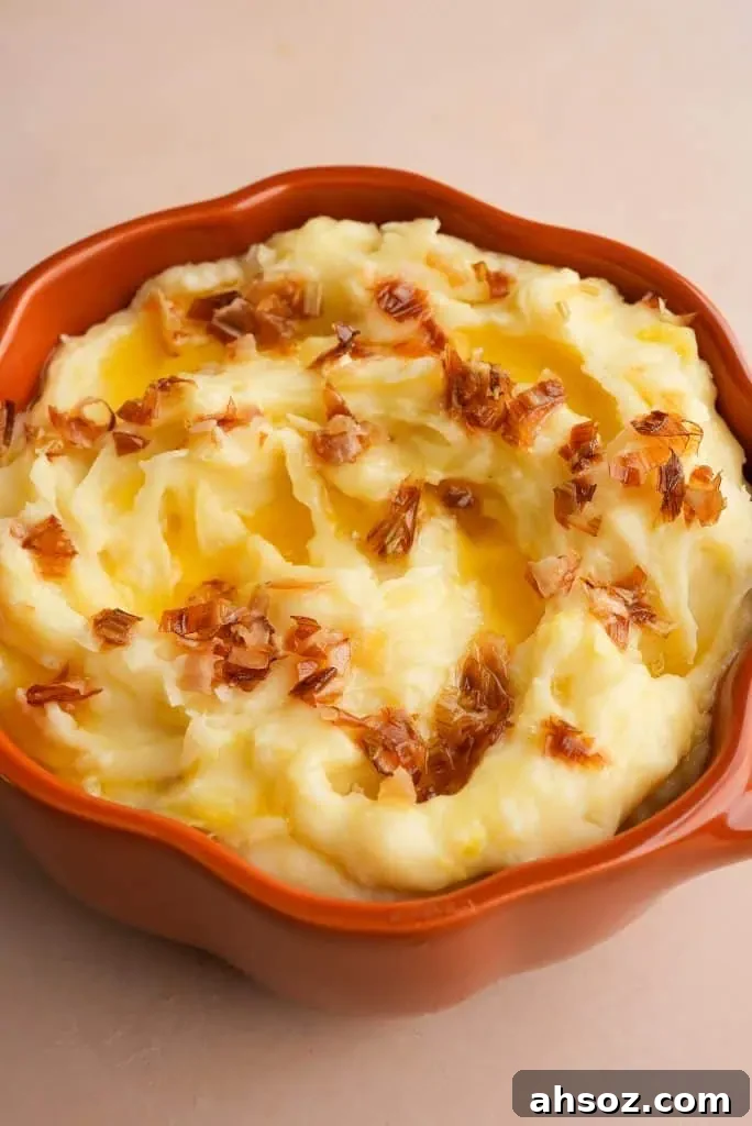 A serving dish filled with creamy mashed potatoes topped with golden roasted leeks and melted butter.
