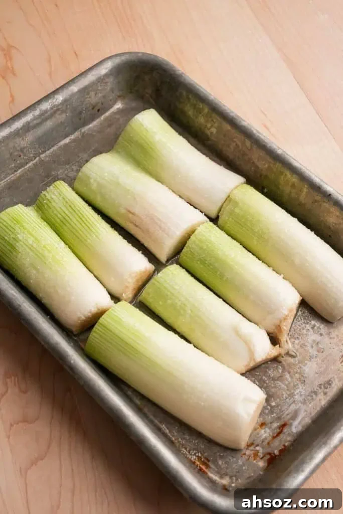 Halved leeks on a baking tray, seasoned and ready to roast in the oven.