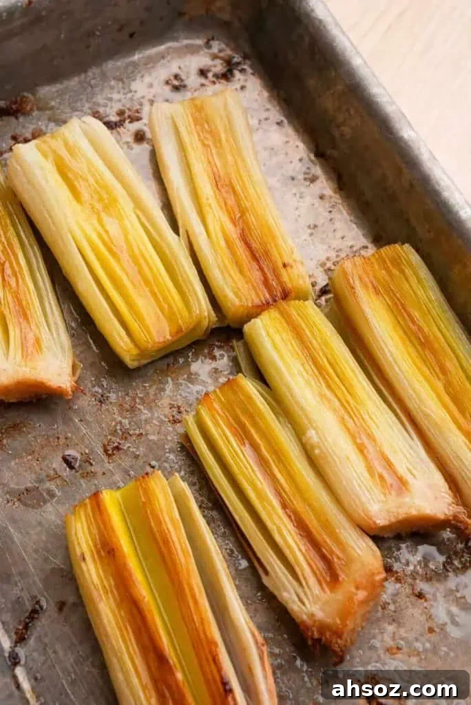 Roasted leeks laid out on a baking sheet, lightly browned and tender.