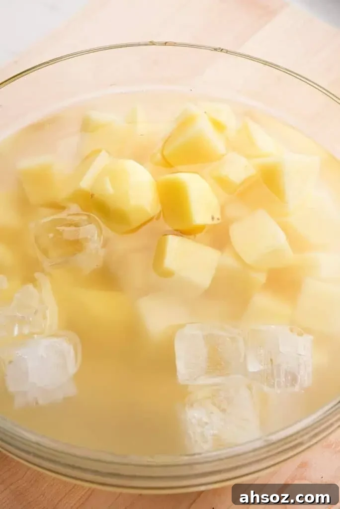Peeled and cubed potatoes soaking in a bowl of ice water before boiling.