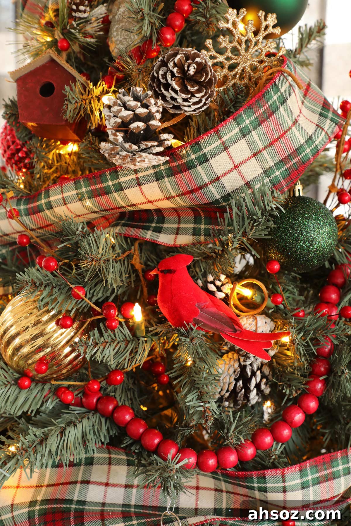 A close-up of a Christmas tree with plaid ribbon, red beaded garland, and a red cardinal ornament.