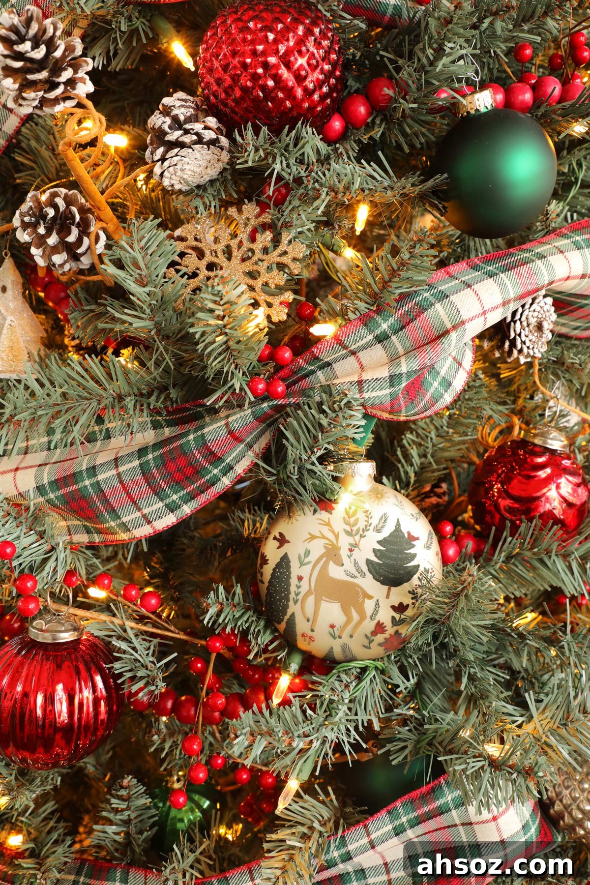 A close-up of a Christmas tree with plaid ribbon, red beaded garland, pine cones, and detailed ornaments.
