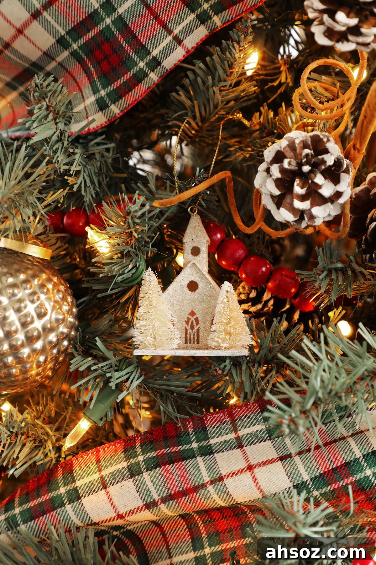 A white glitter church ornament hanging on a Christmas tree.