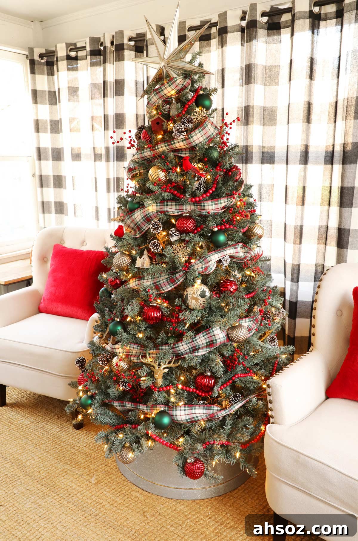 A red and green Christmas tree with plaid ribbon and mercury glass ornaments between two tan chairs in front of buffalo check curtains.