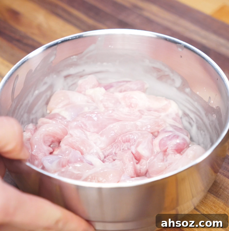 Thinly sliced raw chicken thighs marinate in a bowl with cornstarch, shaoxing wine, and salt, ready to be stir-fried for yaki udon.