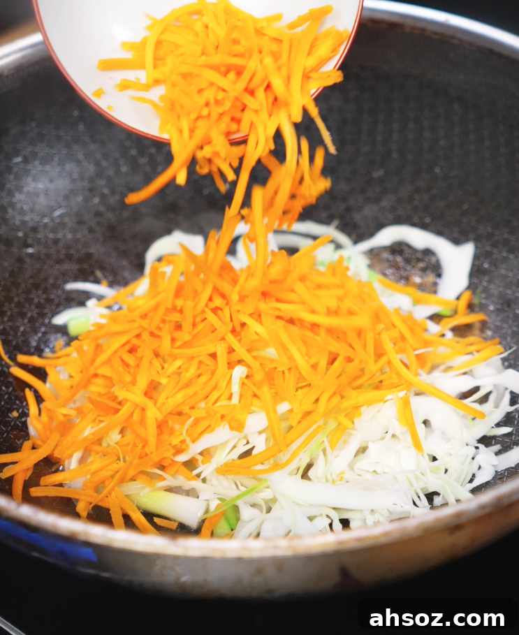 Shredded carrots and sliced cabbage are added to a hot pan of onions and scallions to create a colorful veggie mix for the stir-fry.