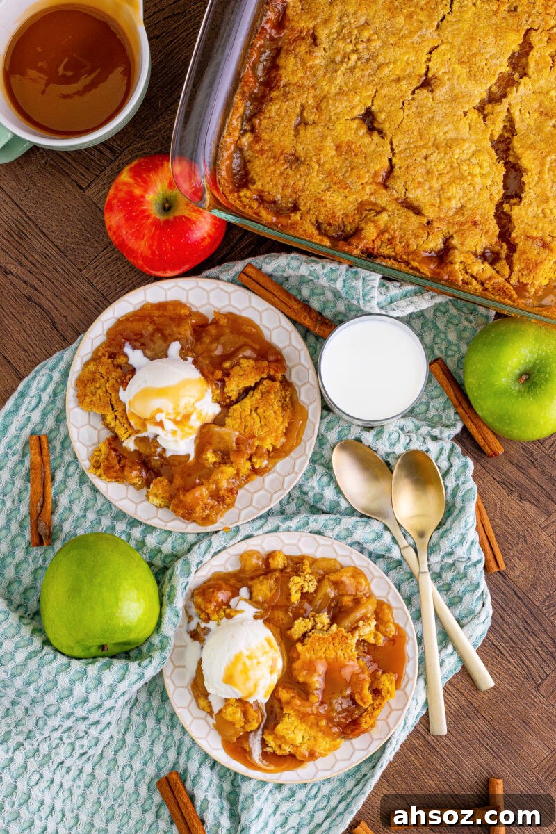 lookign down at two plates of caramel apple dump cake with ice cream next to the baking dish and whole apples