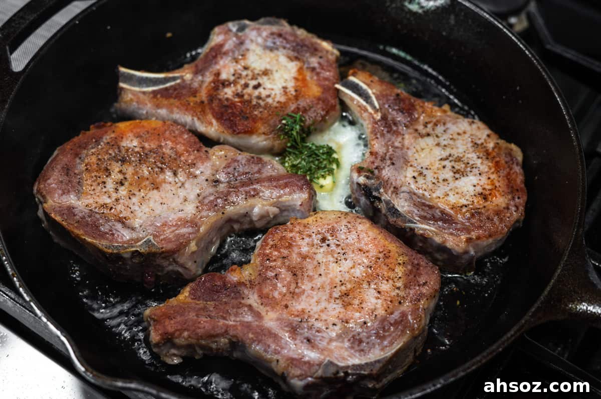adding butter and rosemary to pork chops in cast iron skillet.