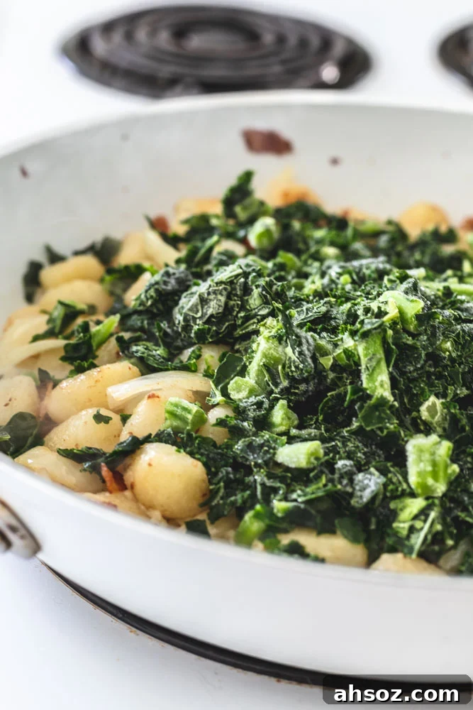 Bacon, onions, gnocchi and kale cooking in a skillet.