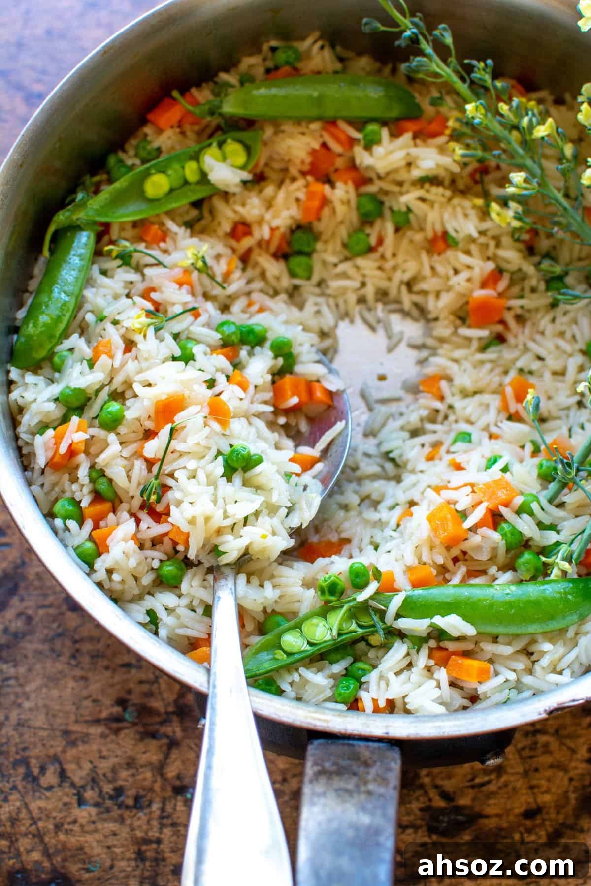A close up of a pot of Arroz with peas and carrots with a spoon in the pot and several whole sugar snap peas in the pot. 
