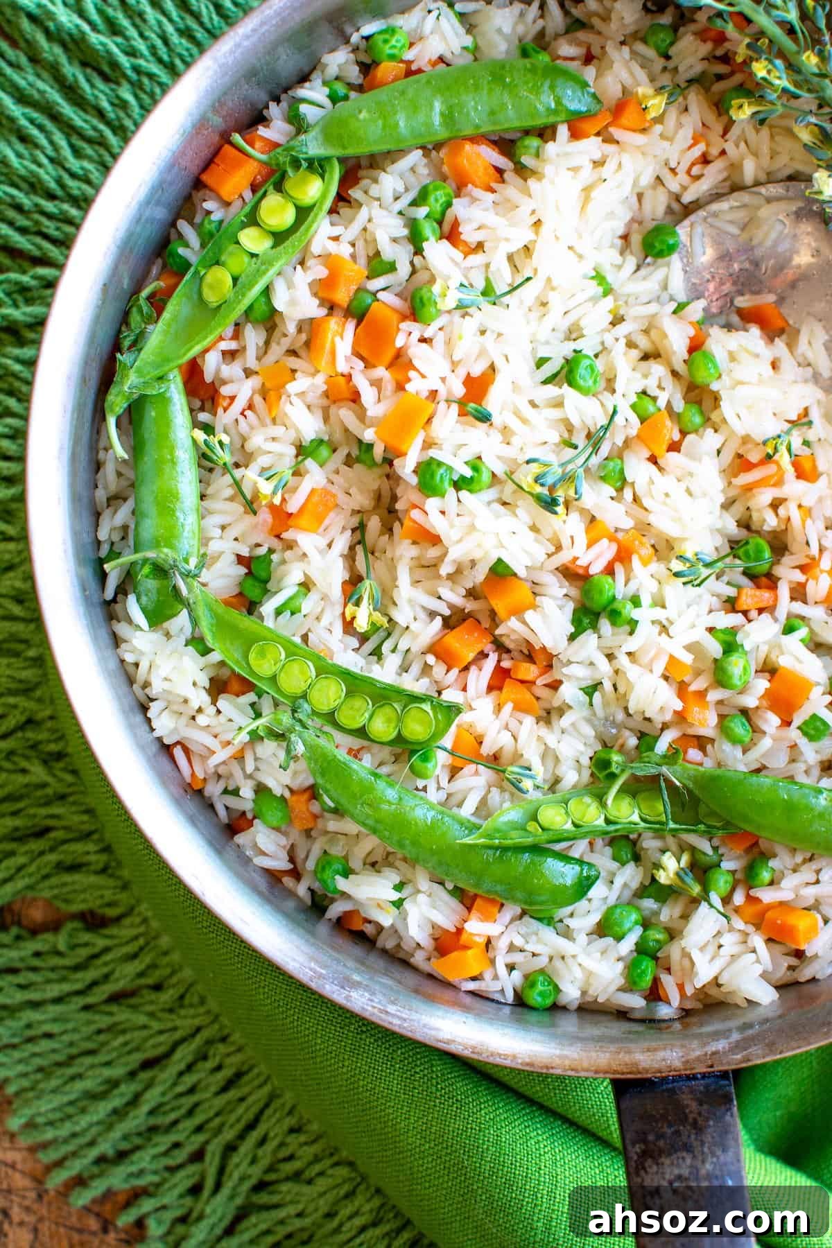 A close up of a pot of Arroz with carrots and peas sitting on a green tablecloth. There is a spoon sticking in the pot. 