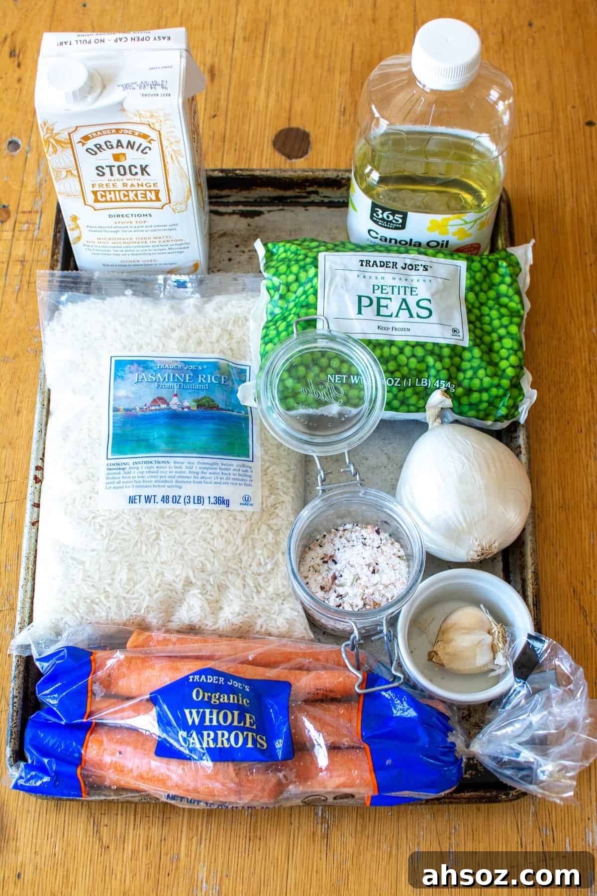 All the ingredients to make arroz including Jasmine rice, canola oil, chicken broth, frozen peas, carrots, onion, and garlic. 