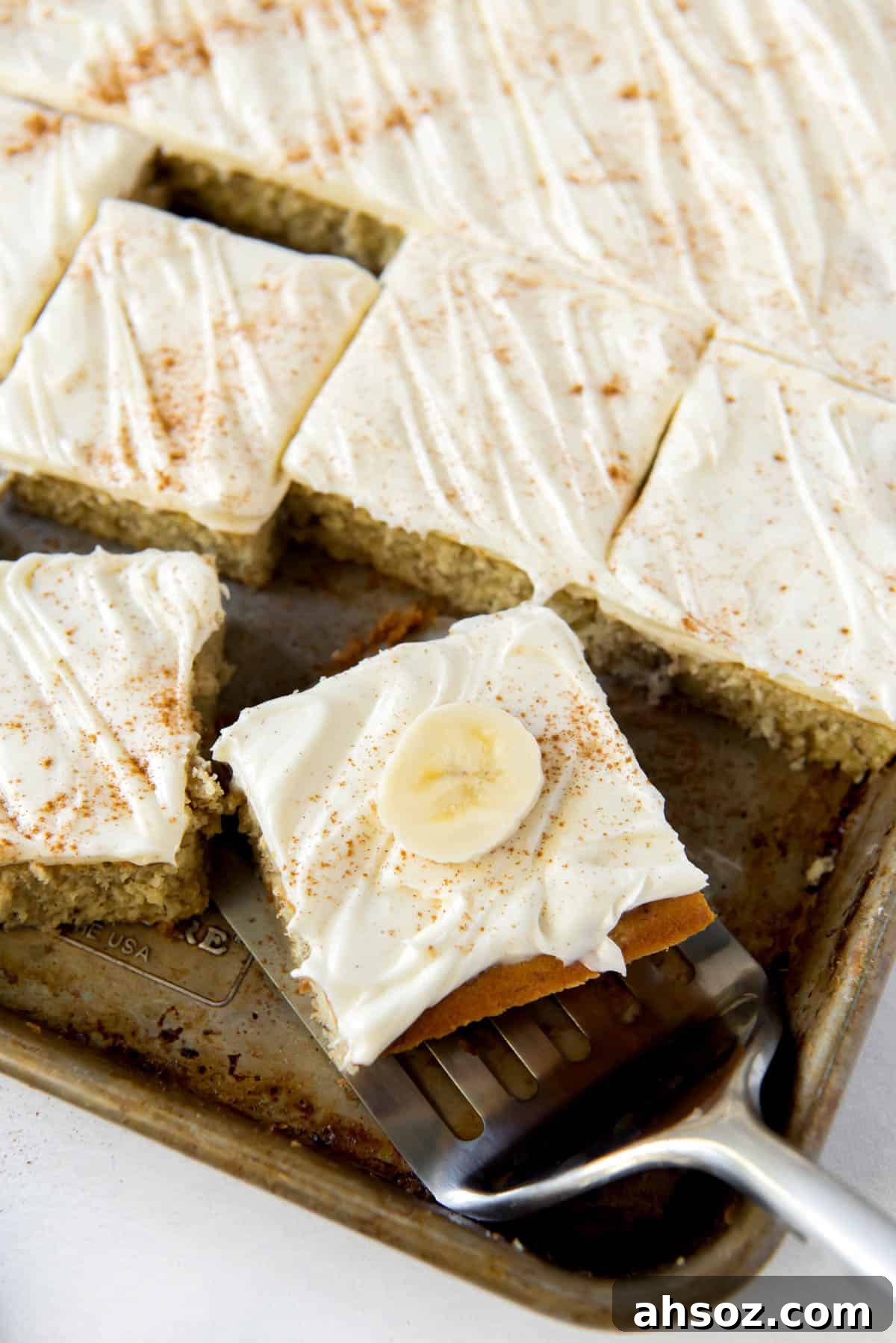 Banana bars with cream cheese on a sheet pan, one slice being served.
