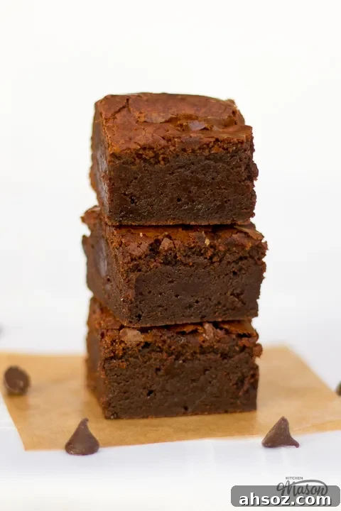 3 ultimate chocolate brownies in a stack on a sheet of baking paper.