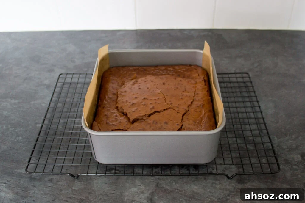 Baked chocolate brownie in a lined tin on a wire cooling rack.
