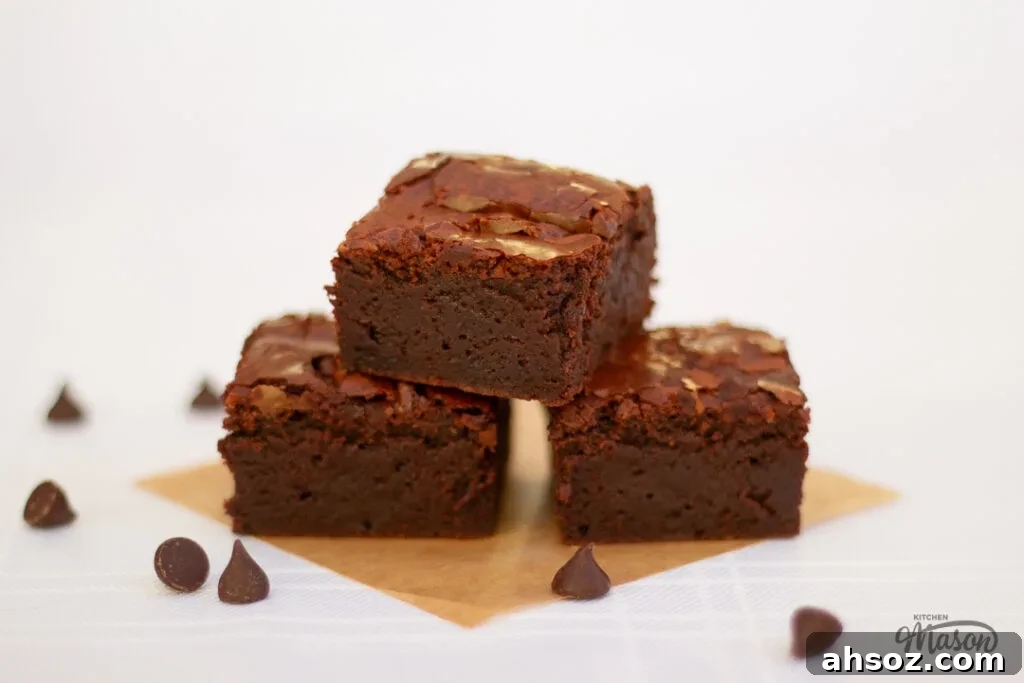 3 ultimate chocolate brownies on baking paper with chocolate chips at the side.