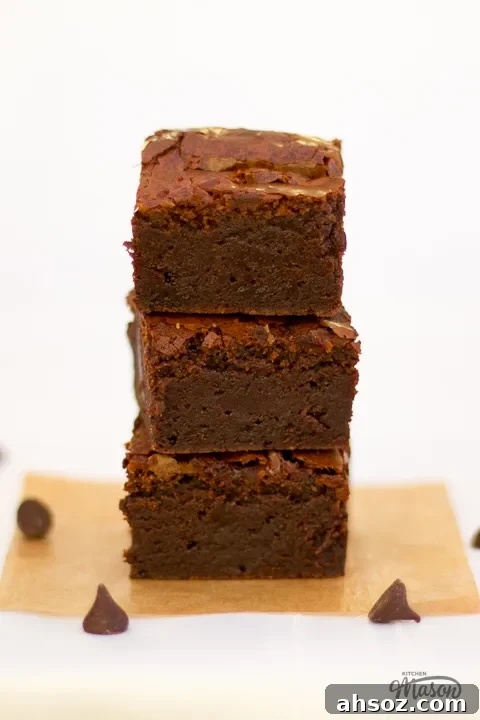 Fudgy ultimate chocolate brownies in a stack with chocolate chips scattered around.