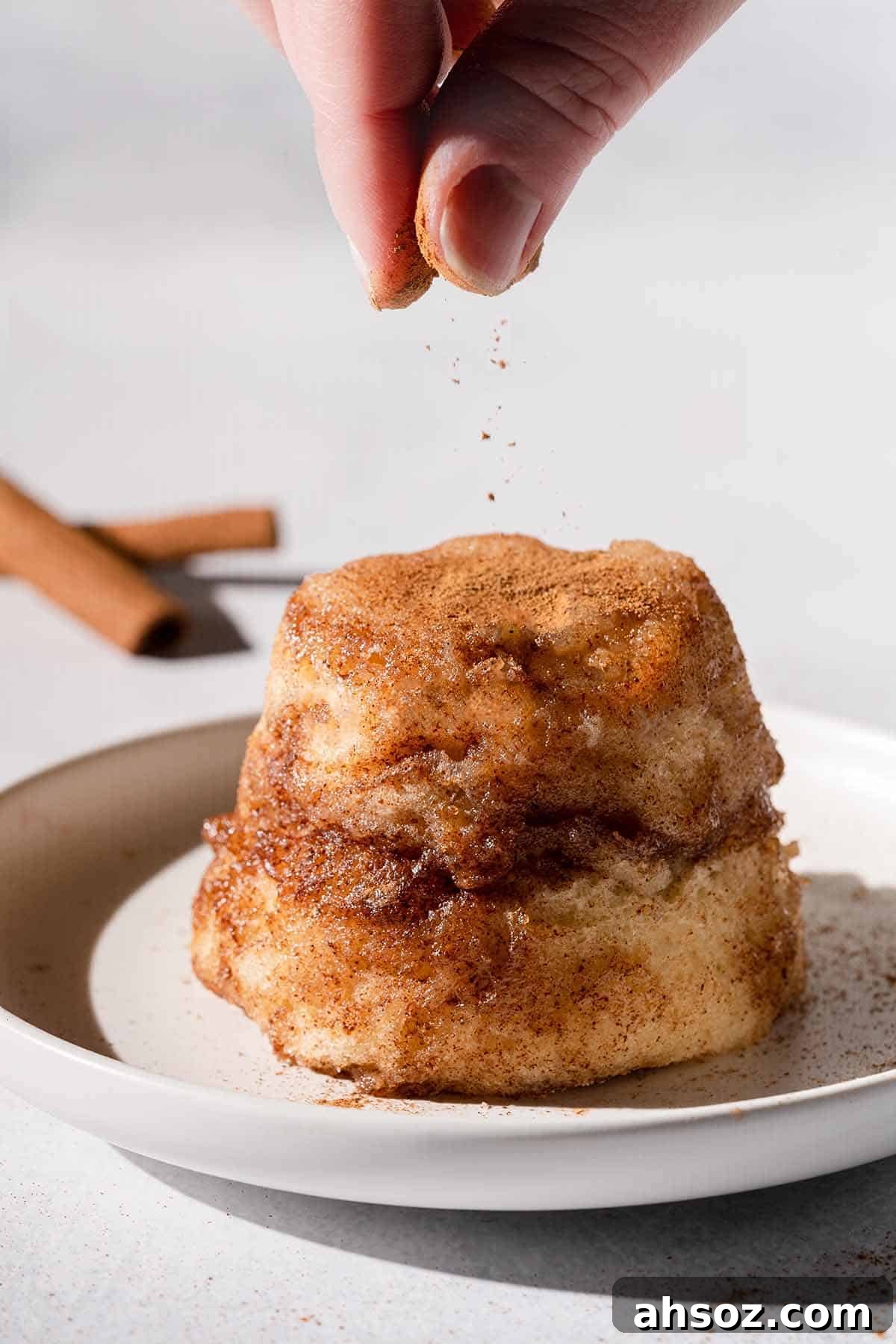 Hand sprinkling cinnamon overtop snickerdoodle mug cake