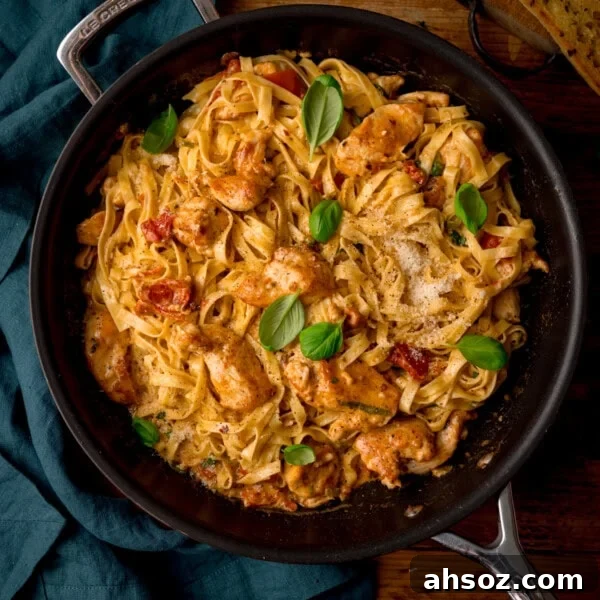 A square, overhead shot of Marry Me Chicken Pasta in a black pan. To the left of the pan, there is a teal napkin tucked beside it. This is all set on a wooden surface.