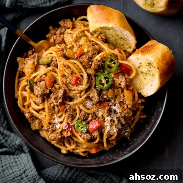 A square, overhead shot of Buffalo Minced Beef Spaghetti in a black bowl with garlic bread and a fork.