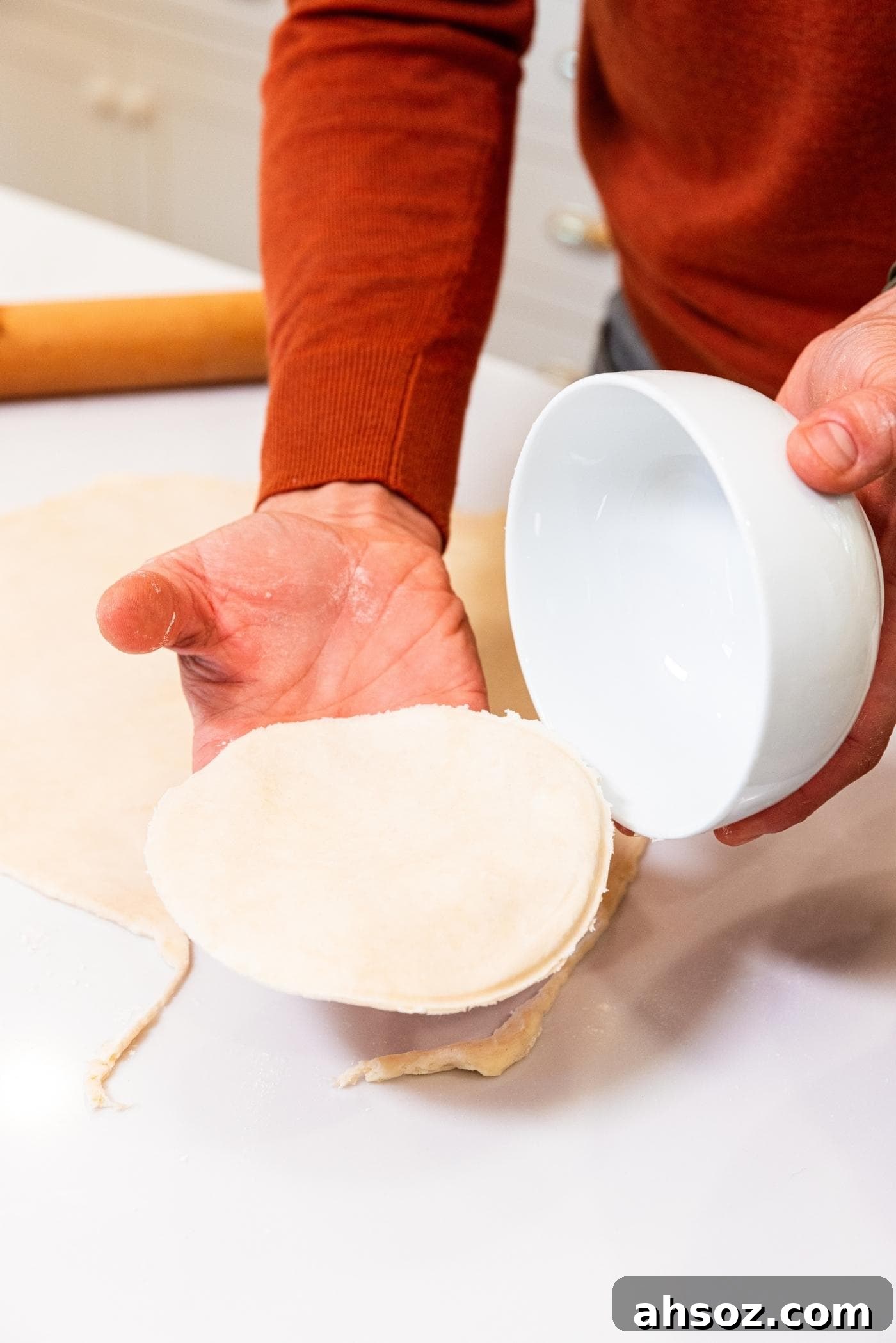 Hand pulling white bowl off of round of dough after being sliced from rest of dough with white countertop underneath.