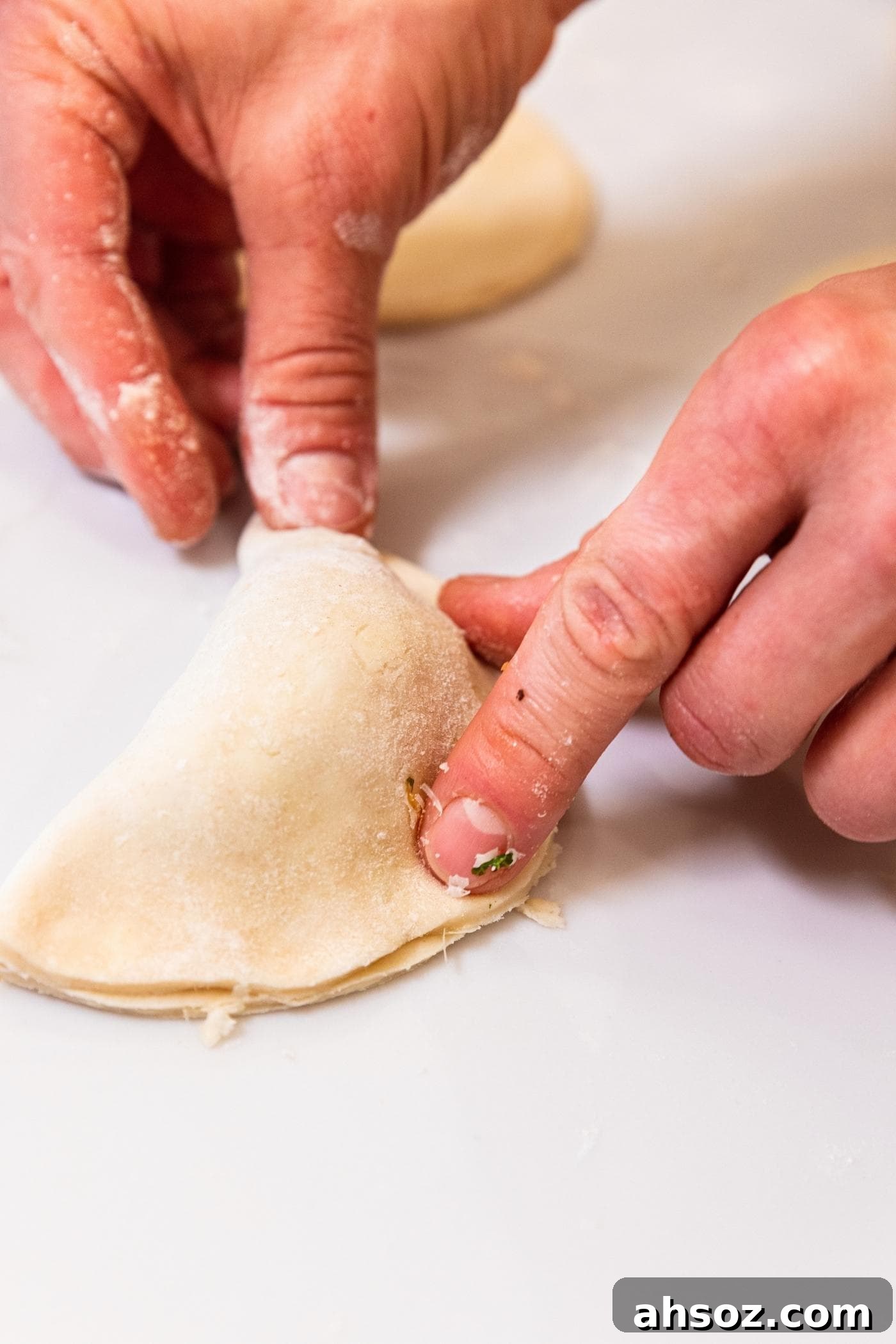 Hand pressing down sides of half moon shaped hand pie filled with butternut squash mixture all on white countertop.