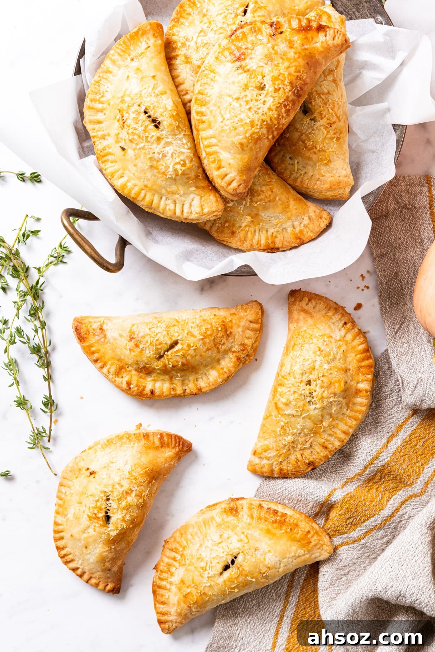 Marble surface filled with lots of baked hand pies that are golden in color with fresh thyme to the side.