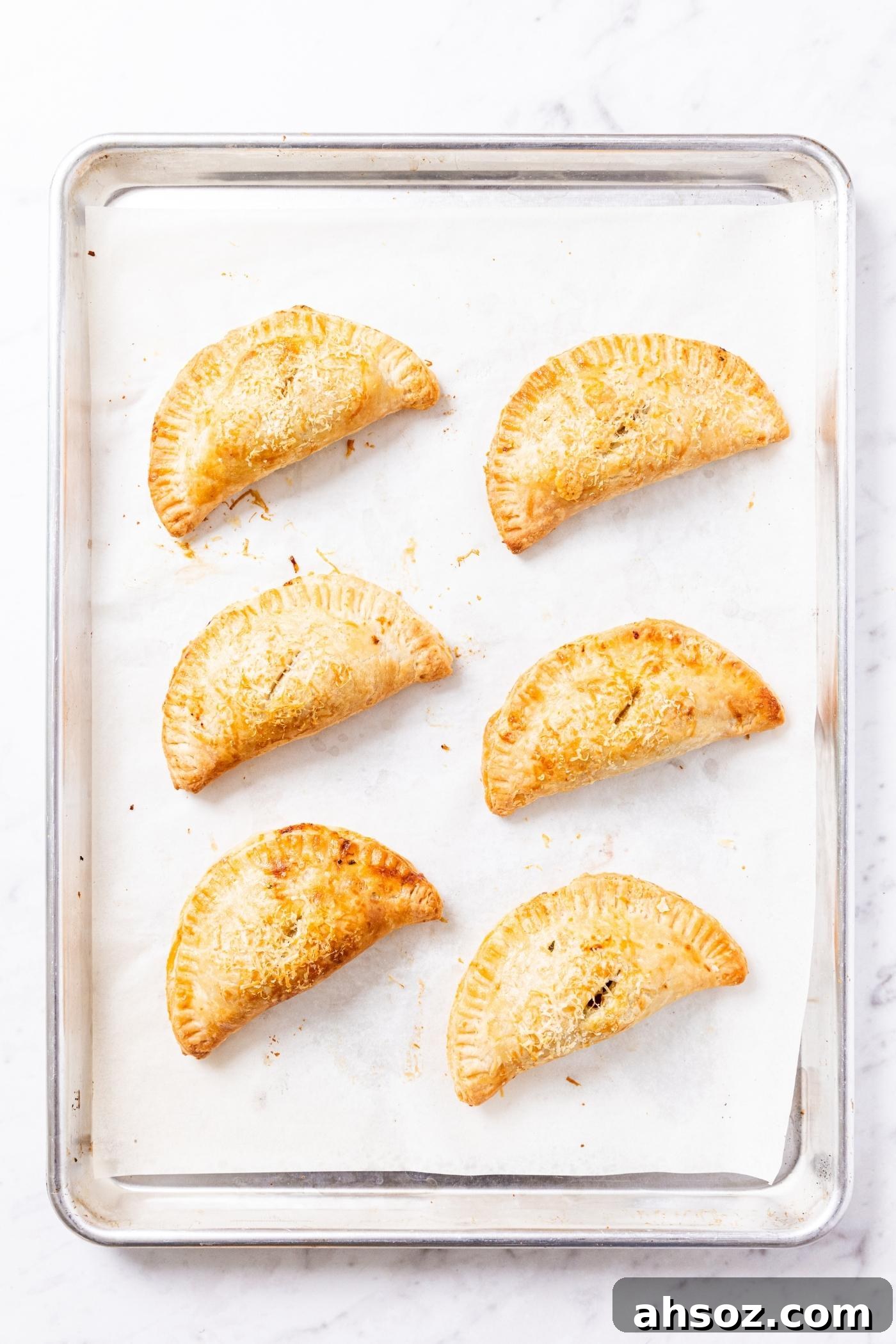 Six hand pies sitting on parchment-lined baking sheet after coming out of oven.