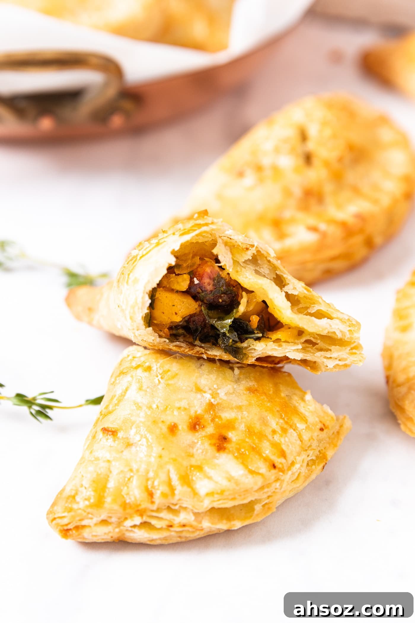 Marble surface with baked hand pie cut in half with one half sitting on top of the other showing the inside filled with butternut squash and sausage mixture with more hand pies in background.