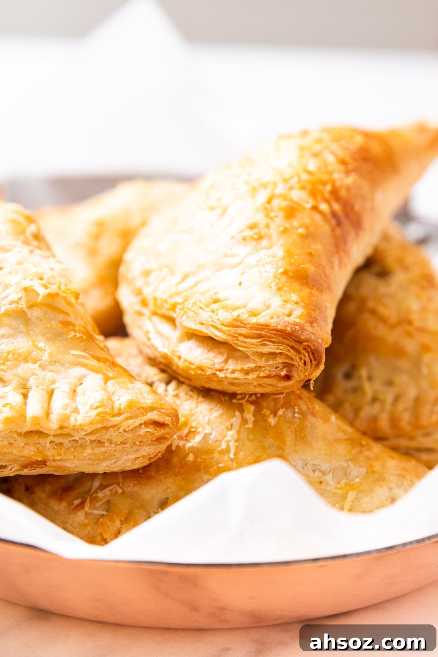 Baked hand pies sitting on top of each other in copper pot sitting on marble surface.