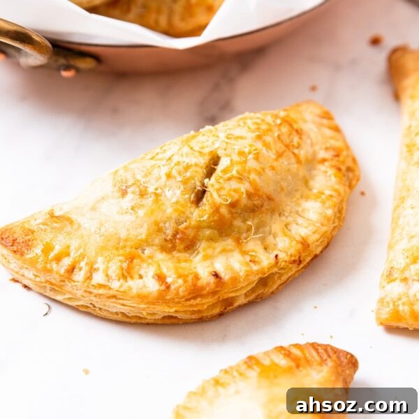 Savory squash hand pie sitting on marble surface after being browned in the oven while baking with more hand pies to the side and in background.