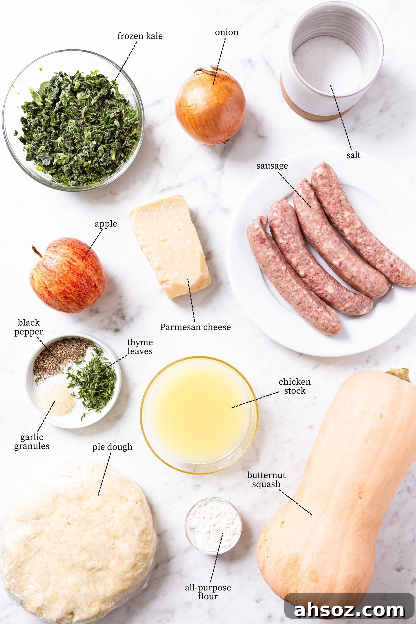 Marble surface filled with all of the ingredients needed to make savory squash hand pies including butternut squash, sausage, kale, pie dough, spices, and more.