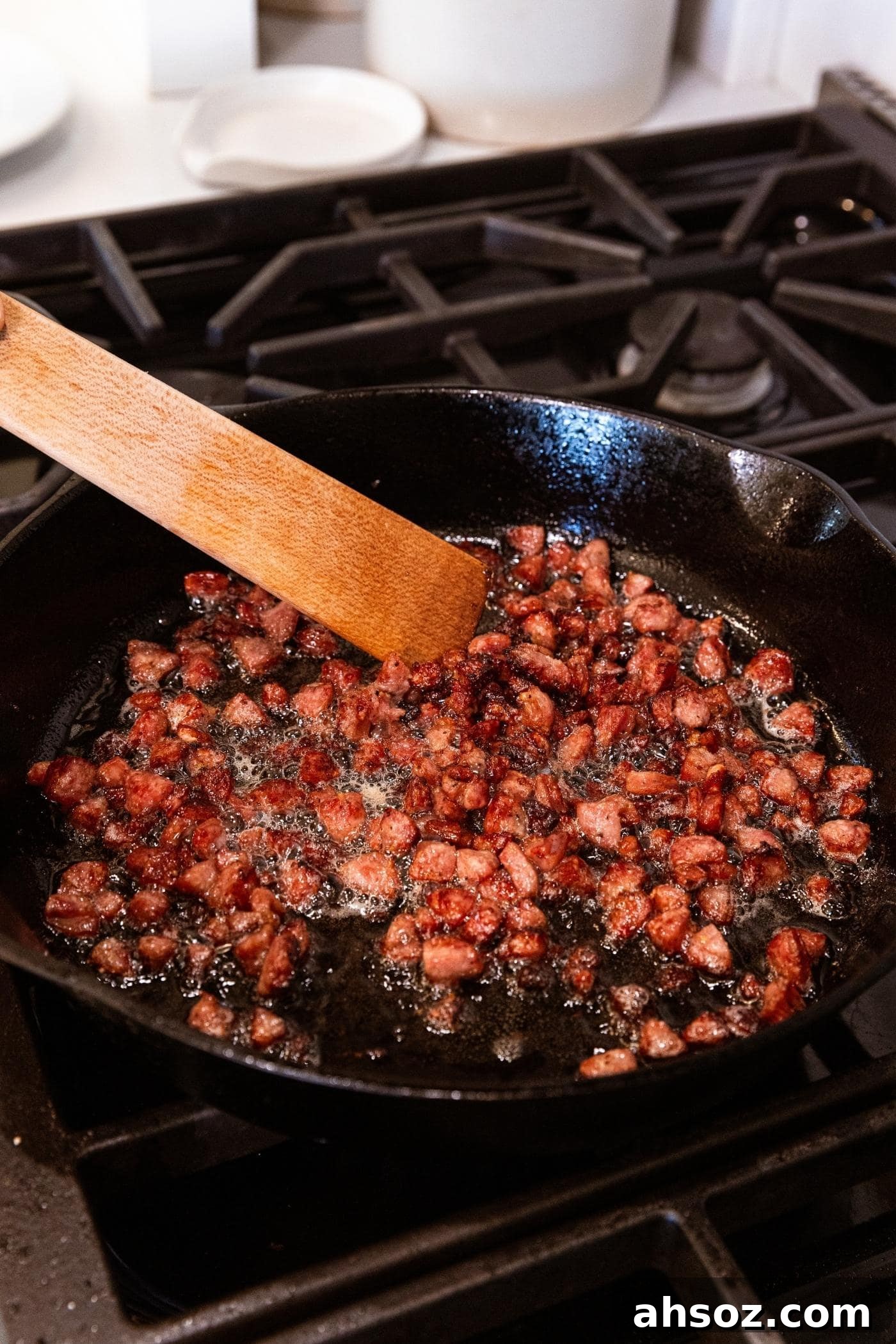 Wooden spatula mixing cooked sausage cut into a small dice in cast iron skillet on stovetop.
